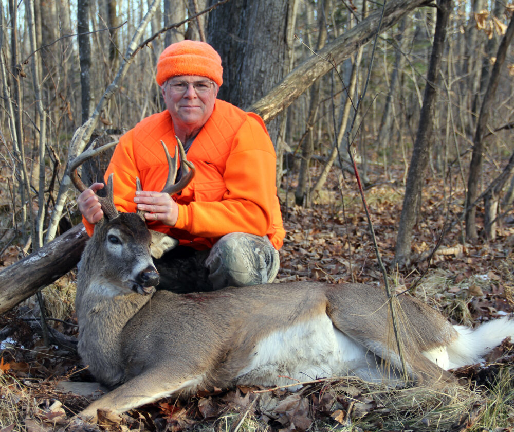 Deer hunter in blaze orange in the woods holding a ten point whitetail buck